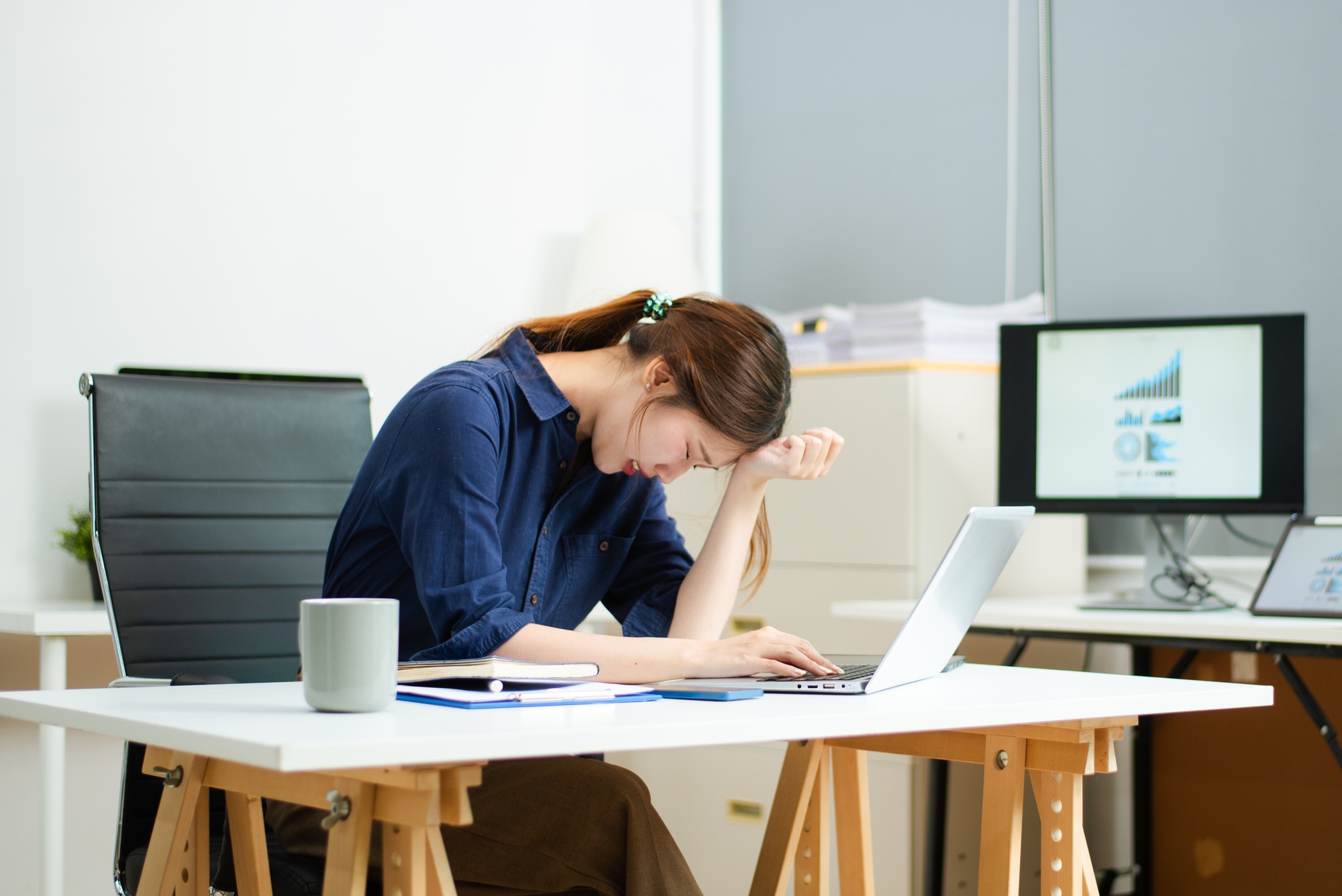 young businesswoman overwhelmed at desk with laptop, charts, and reports. stress, burnout,